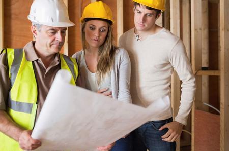 A builder and young couple in their 20s looking at building plans for their new home