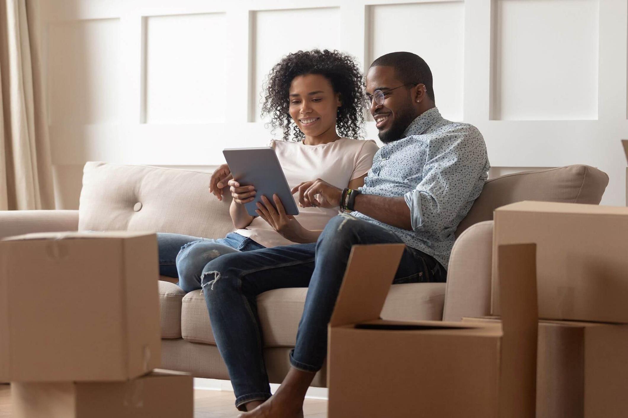 Young couple in their 30s looking at a laptop on a sofa. They are searching for a quality builder to renovate their home.